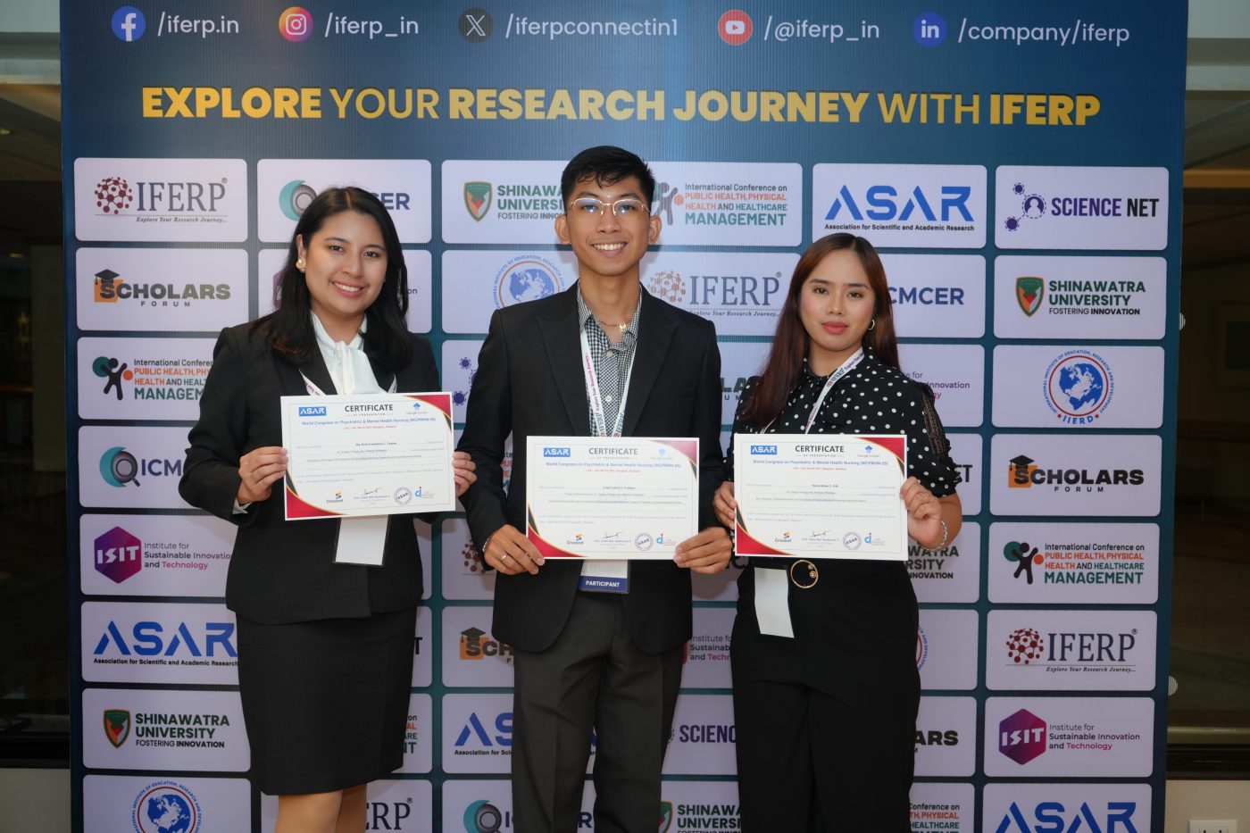 Three delegates holding their presentation certificates in front of the IFERP backdrop